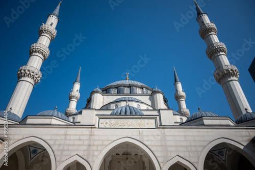 A powerful low-angle exterior shot of Mosque of Namazgah in Tirana, Albania, highlighting its main dome, numerous smaller domes, and two elegant towering minarets under bright daylight.