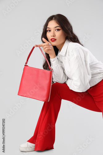 Beautiful young Asian woman in stylish outfit with bag and chair on white bac...