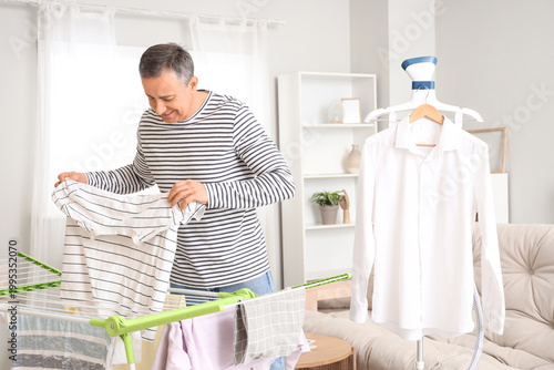 Foto Mature man taking laundry from dryer and steamer at home