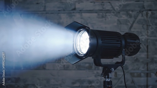 Studio lighting setup with a fresnel light emitting a bright beam against a brick wall backdrop.