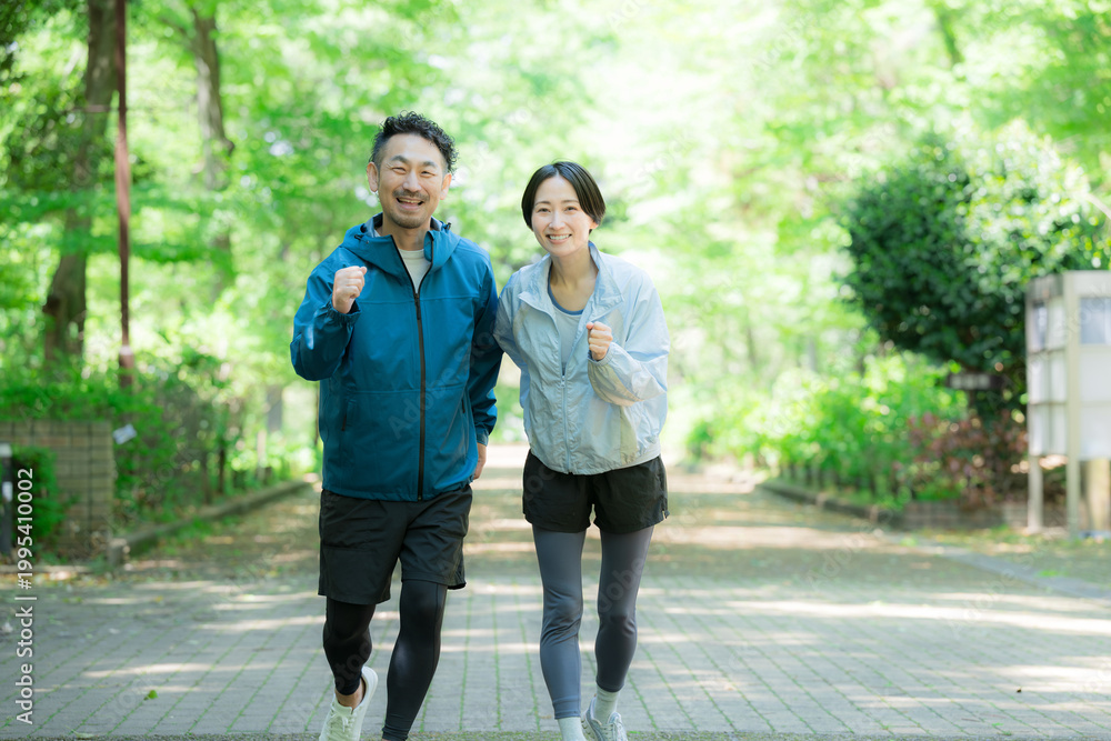 Obraz premium 新緑の公園でウォーキングやランニングのスポーツが楽しいミドル夫婦の正面カメラ目線笑顔 ダイエットや健康などの明るいイメージ全身
