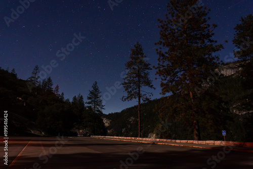 Starry night sky over a mountain landscape with trees.