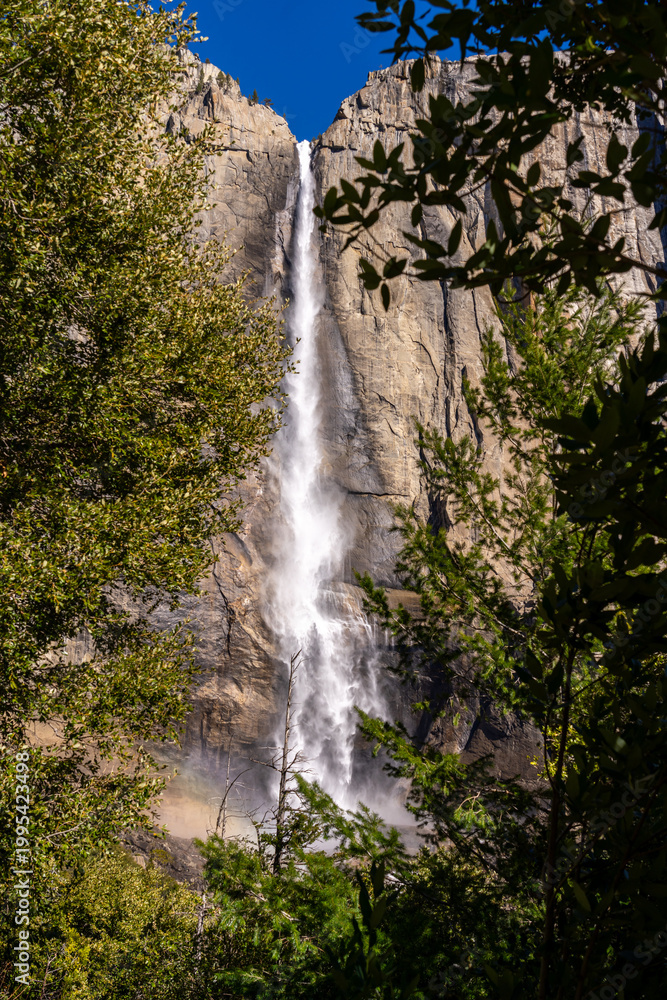 Obraz premium Waterfall cascades down a rocky cliff face, framed by trees.