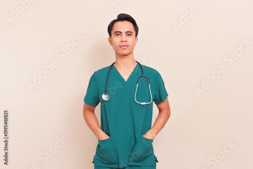 Obraz na płótnie Confident Southeast Asian male doctor in green scrubs with stethoscope and hands in pockets