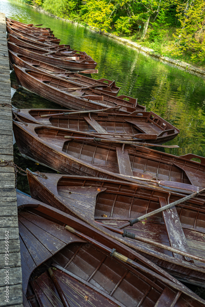 Fototapeta premium Wooden boats at a scenic lake pier. Calm forest lake with wooden boats. Travel destination in Plitvice Lake. Boat on clear water. Tourism and outdoor recreation. Peaceful lakeside vacation.