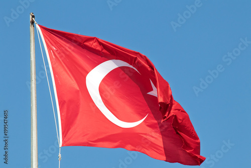 Turkish Flag waving in the blue sky. Red Turkish flag on the flagpole. National holiday. Victory, independence idea concept. Horizontal photo. No people, nobody. Copy space. Left-aligned text.