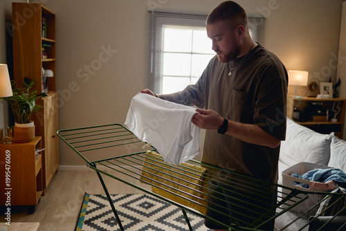 Fotografie Young adult Caucasian man hanging laundry at home, managing daily chores during house arrest and isolation