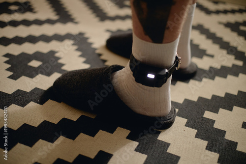Fotografía Close up of young adult man wearing electronic ankle monitor at home, representing house arrest and criminal justice surveillance