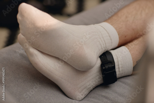 Tableau sur toile Close up of young adult man wearing electronic ankle monitor during house arrest, showing legal surveillance and restricted freedom
