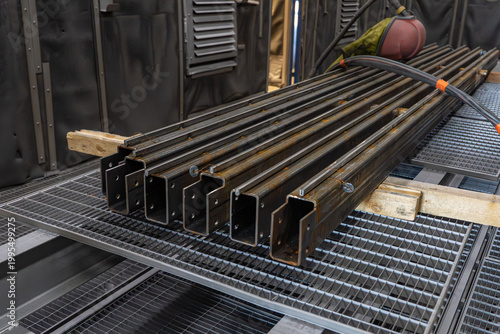 Fotografie Alignement de profilés métalliques en acier sur cales en bois dans un atelier de fabrication pour la préparation de charpentes industrielles