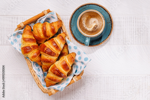 Aromatic croissants in wicker basket with cup of coffee