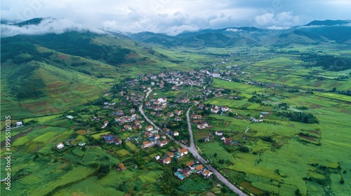 Aerial View of a Serene Rural Landscape Surrounded by Lush Green Fields and Rolling Hills Under a Cloudy Sky with a Small Village