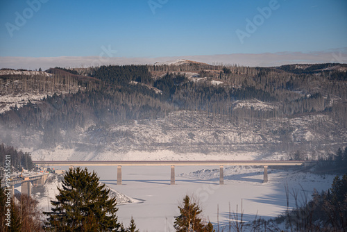 High altitude view of a bridge and snowy mountain slopes with forest damaged by bark beetles