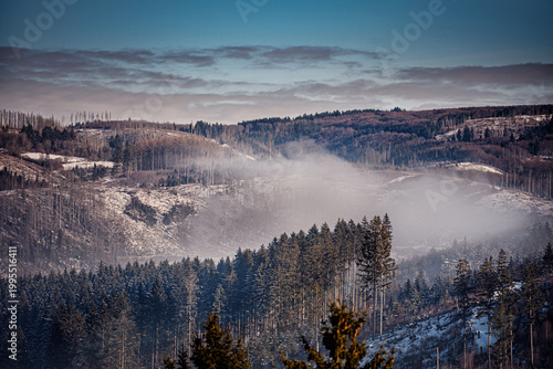 High voltage electricity pylons crossing snowy mountain ridge in winter fog