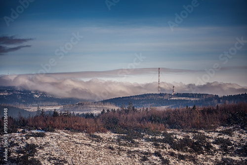 Telecommunication towers on snowy mountain peak with thick fog and dead forest in winter