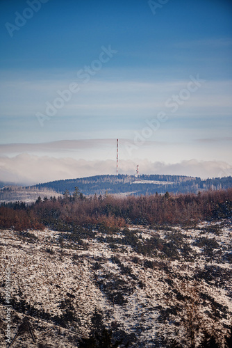 Low angle view of broadcasting tower on mountain summit surrounded by snowy dead forest