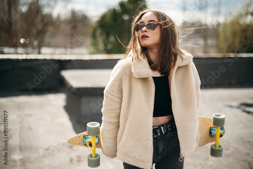 Beautiful woman with skateboard standing on building rooftop