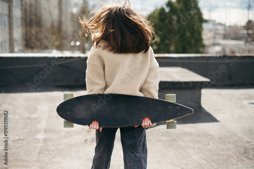 Back view of young brunette posing with skateborad on roof