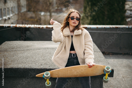 Pretty woman sitting with skateboard on sunlight rooftop
