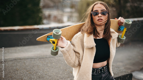Young brunette in sunglasses posing on roof with skateboard