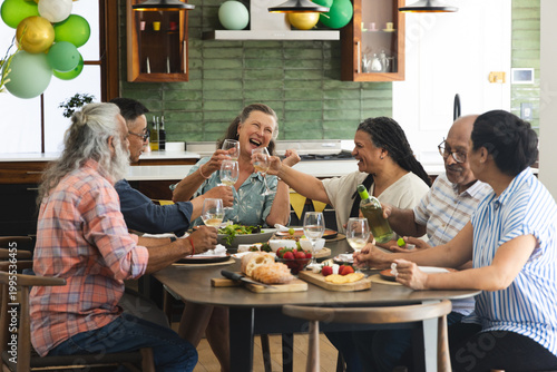 Diverse family with seniors laughing and toasting in home kitchen over wine glasses