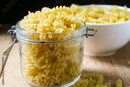 top view of uncooked fusilli pasta in a jar and bowl on a wooden table