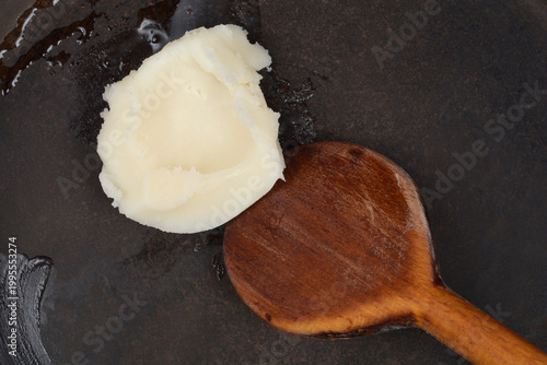 Schilderij op canvas A top down shot of a white dollop of pork lard melting in a dark frying pan with a wooden spoon