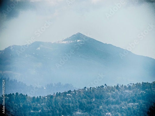 a large mountain peak partially covered in snow, surrounded by a hazy atmosphere