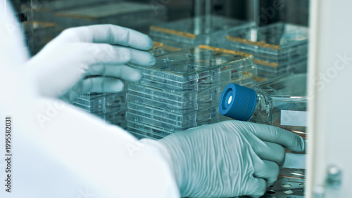 Принти на полотні A researcher in a clean suit carefully handles a vial containing a glowing blue substance in a sterile laboratory environment