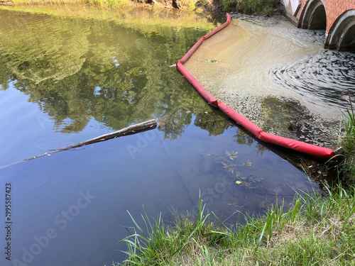 Foto Containment boom holding back foam and pollution in river water near culvert