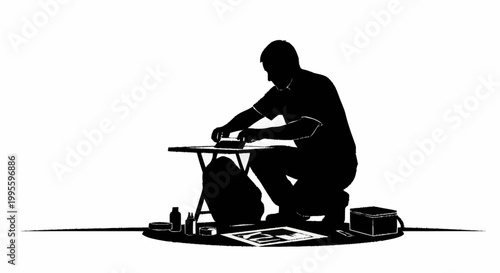 A crouching man meticulously working on a craft project with supplies.