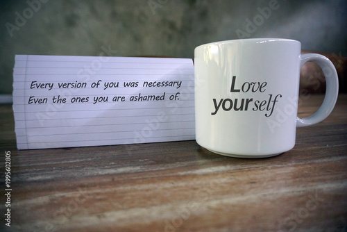 Inspirational motivational quote - Every version of you was necessary. Even the ones you are ashamed for. Love yourself. With text reminder on white empty cup and notepaper on the table. Self care.