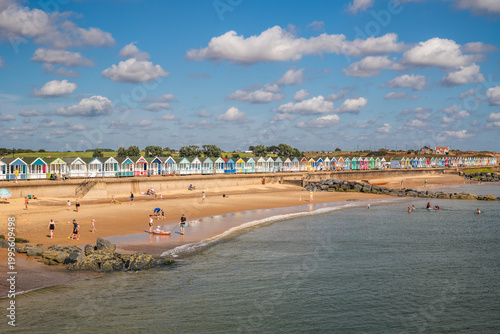 A charming seaside scene in Southwold, where colourful beach huts and families on the sand backdrop capture the relaxed essence of a classic British coastal day