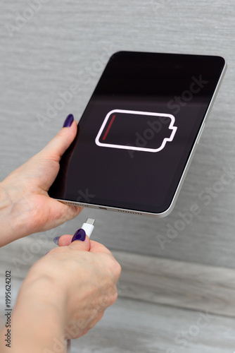 A woman charges a tablet, vertical photo. Close-up of a woman's hands charging a tablet using a cable and USB port. dead tablet battery. tablet on charge. Vertical photo