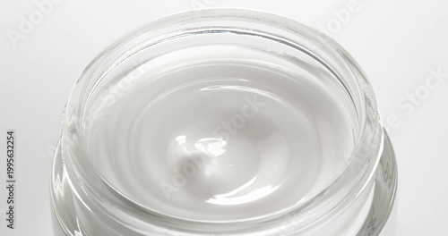 Open jar with cosmetic facial cream close-up on a rotating table.