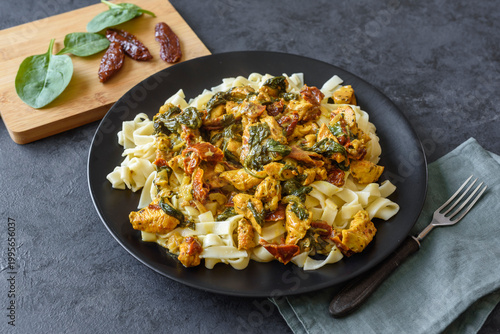 Pasta with chicken, spinach and dried tomatoes in turmeric sauce