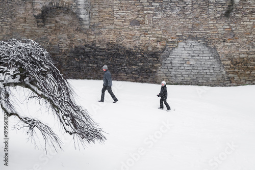 Tallinn, Estonia - 03 January 2025: View of people traversing the snow-covered grounds near the imposing stone walls, a stark contrast of cold stone and the soft, enveloping snow.