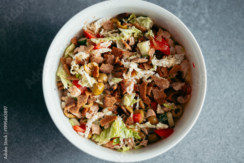 Фотография A bowl contains a colorful mix of fresh vegetables, cooked chicken pieces, and crunchy toppings
