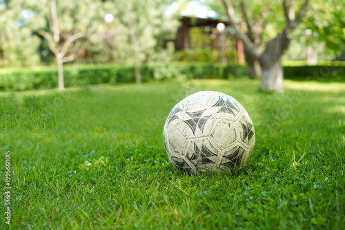  worn, classic soccer ball sits on a vibrant green lawn with copy space to the left, set against a sunny, blurred garden background.