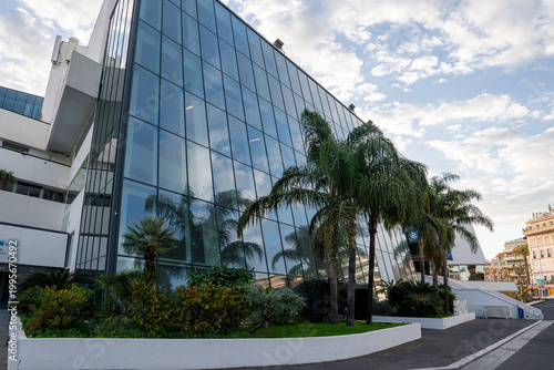 Foto Palais des Festivals et des Congres in Cannes, France stands with a sharply slanted facade, palm trees, curving promenade, white terraced ramps, and soft daylight skies