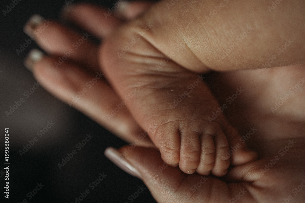 Fototapeta premium Mother holding newborn baby foot in hands, tender moment, close-up detail of tiny toes