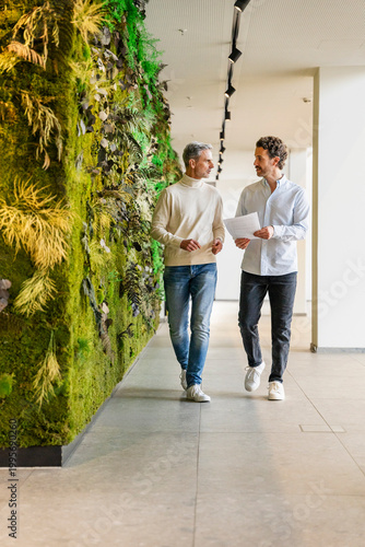 Two men walking and discussing business in a modern office with a green wall
