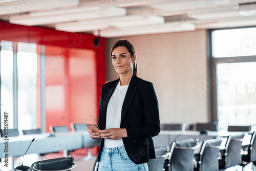 Businesswoman with smart phone standing in conference room at office