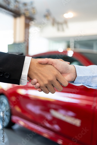 Close-up of a professional handshake in a car dealership. Successful vehicle purchase deal between dealer and client. Automotive sales and service concept. Vertical Shot