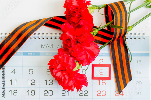 9 May background, red carnations and St George ribbon lying on the calendar with framed 9 May date