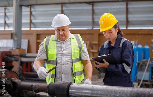 In an industrial plant, a supervisor is measuring metal pipes with a tape measure while a technician records the data, emphasizing accuracy, inspection, and quality control.