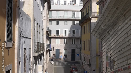 narrow street in Lisbon, Portugal with pedestrians and tuktuk passing by