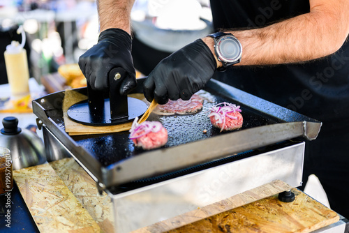 Chef preparing smash burgers on a flat top grill, adding toppings to freshly cooked beef patties with melted cheese, capturing street food cooking process and professional burger preparation in a