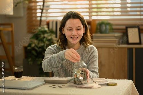 Fotografie Young Caucasian woman putting coins into a jar, representing saving money and bu
