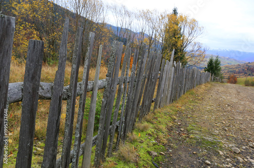 Rustic wooden fence lines a winding dirt road through autumn mountain scenery